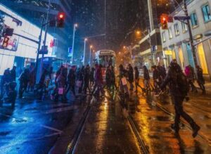 A crowd of people walk through a snowy night on a Toronto street with a streetcar in the background.