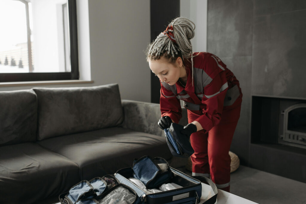 A young woman with dreadlocks wears black gloves as she packs a suitcase.
