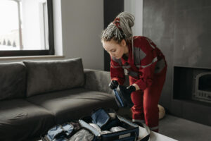 A young woman with dreadlocks wears black gloves as she packs a suitcase.